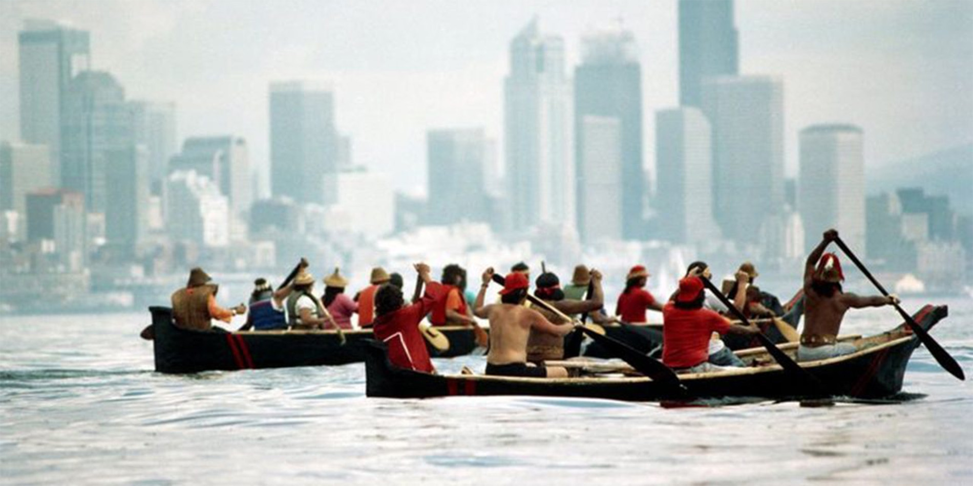 people in canoes with city skyline in distance