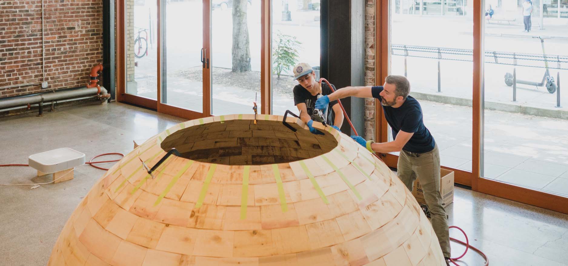 Two men building a cedar dome for an art installation.